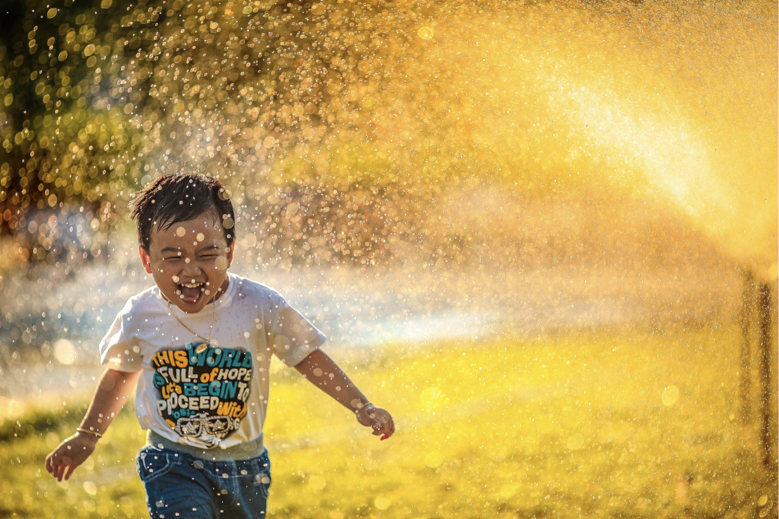 happy boy child running in sprinkler
