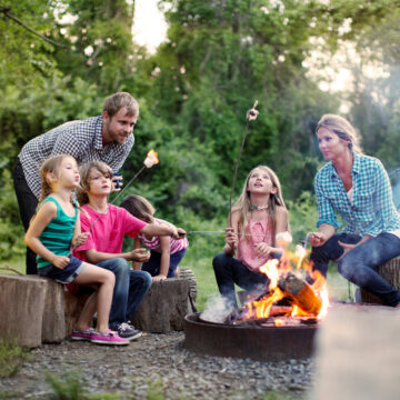 Family roasting marshmallows while camping in forest