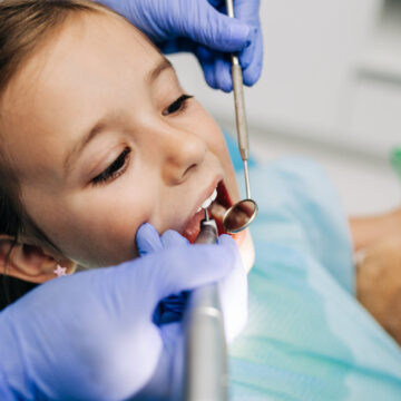 Cute little girl sitting on dental chair and having dental treat