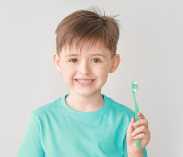 Portrait of little boy brushing teeth on light background