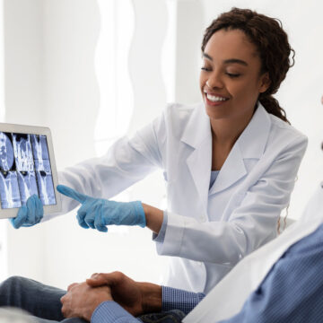 Smiling african female dentist showing patient teeth xray