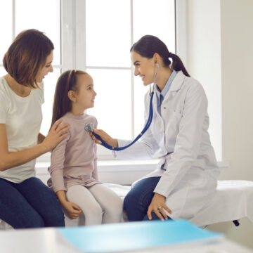 Mother and child seeing family practitioner. Smiling pediatrician with stethoscope checking little girl's lungs. Friendly doctor listening to young patient's breath or heartbeat during medical exam