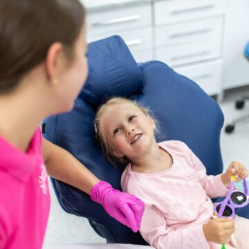 Happy child at first pediatric dental appointment with smiling dentist