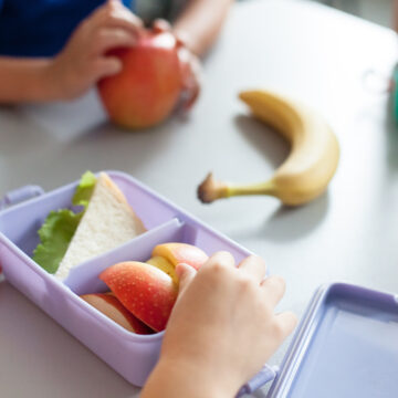 School kids eating healthy food from packed lunch boxes. Children sit at table in cafeteria. Pupils have vegetarian breakfast in canteen. Back to school concept. Lifestyle moment in elementary college